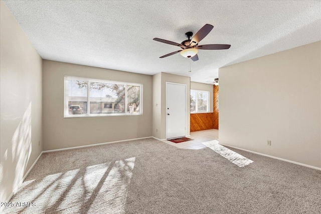 unfurnished room with light colored carpet, ceiling fan, a textured ceiling, and baseboards