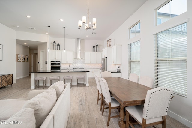 dining space with light wood-type flooring, baseboards, visible vents, and a chandelier