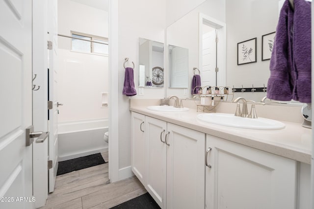 bathroom with wood finished floors, a sink, toilet, and double vanity