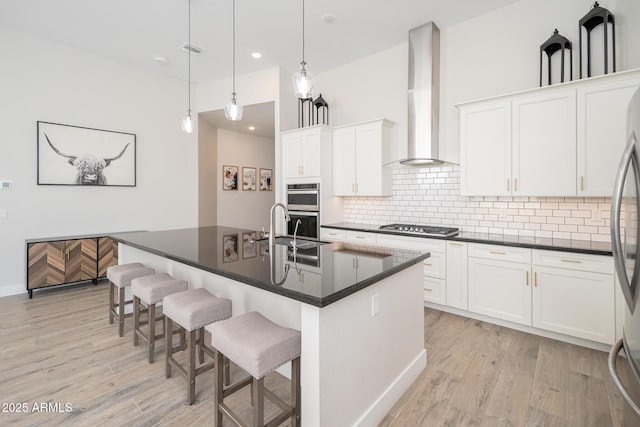 kitchen with tasteful backsplash, dark countertops, light wood-style floors, a sink, and wall chimney range hood