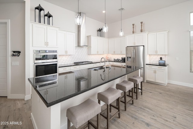 kitchen with stainless steel appliances, wall chimney exhaust hood, a sink, and white cabinets