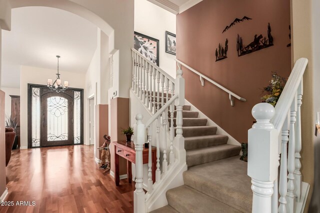 foyer featuring arched walkways, a notable chandelier, wood finished floors, baseboards, and stairs