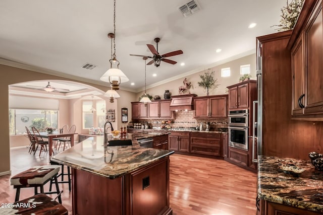 kitchen featuring visible vents, dark stone countertops, a center island with sink, and pendant lighting