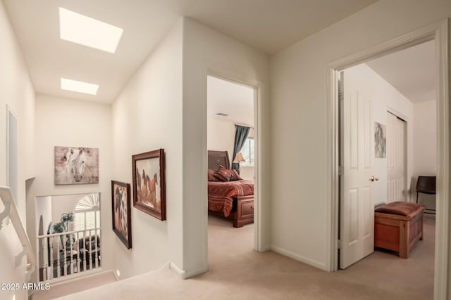 hall with light carpet, a skylight, an upstairs landing, and baseboards