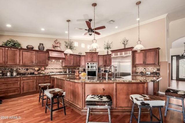 kitchen featuring visible vents, arched walkways, hanging light fixtures, a kitchen island with sink, and stainless steel appliances