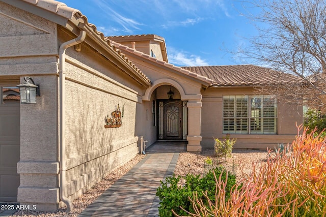 doorway to property with a garage, a tile roof, and stucco siding