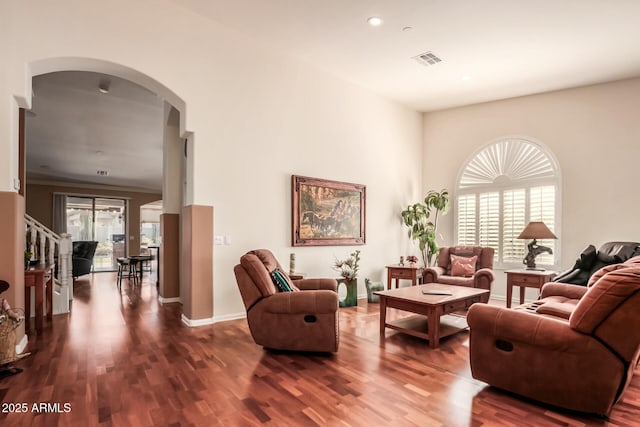 living room featuring arched walkways, a healthy amount of sunlight, visible vents, and dark wood finished floors