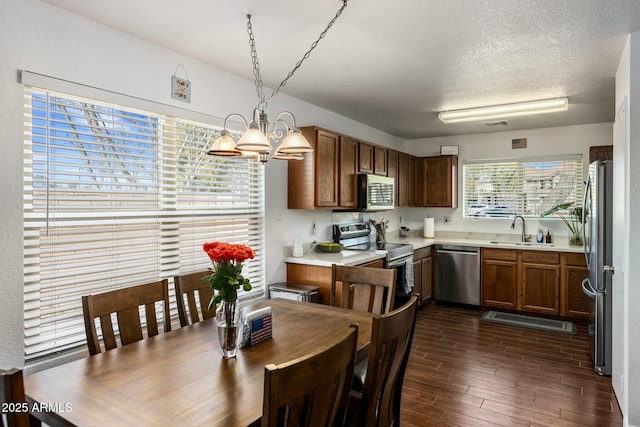 kitchen with sink, appliances with stainless steel finishes, dark hardwood / wood-style floors, decorative light fixtures, and a chandelier