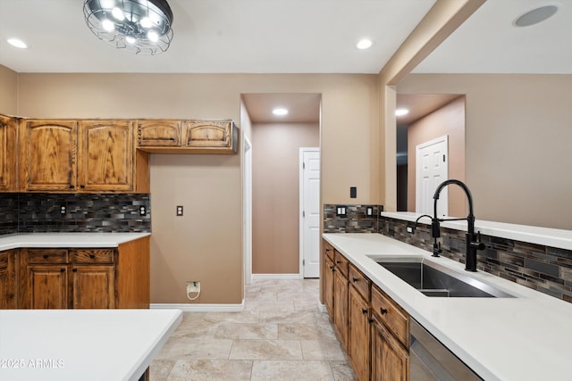 kitchen featuring stainless steel dishwasher, light countertops, brown cabinetry, and a sink