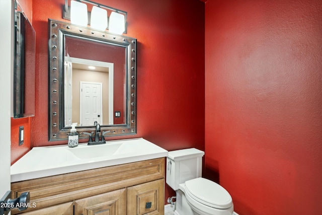 bathroom with vanity, toilet, and a textured wall