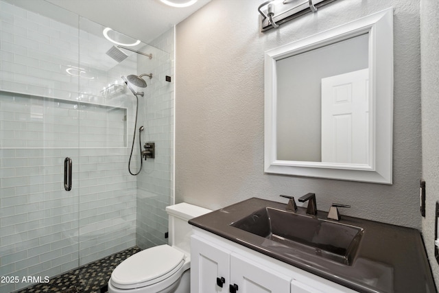 full bathroom with vanity, a shower stall, toilet, and a textured wall