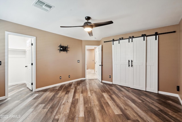 unfurnished bedroom with visible vents, baseboards, a barn door, and wood finished floors