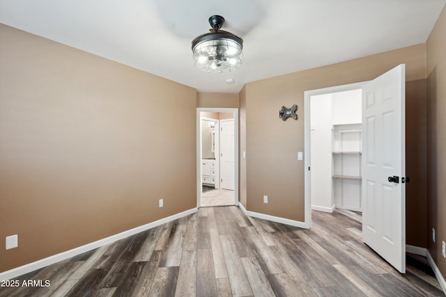 unfurnished bedroom with a walk in closet, ensuite bath, wood finished floors, and baseboards