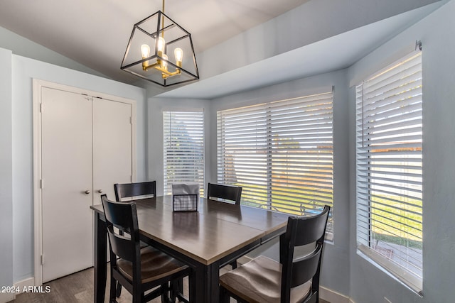 dining space with hardwood / wood-style floors, vaulted ceiling, and a notable chandelier