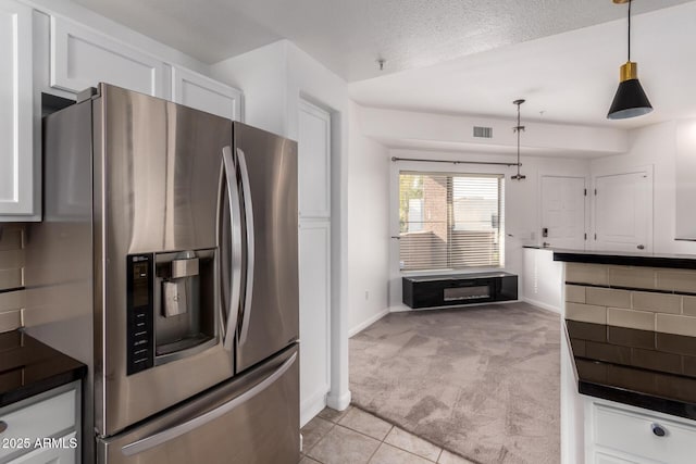 kitchen with stainless steel fridge, white cabinetry, hanging light fixtures, backsplash, and light carpet