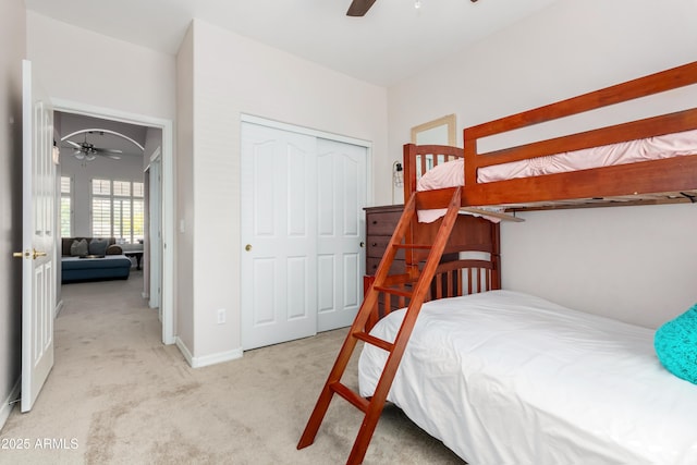 bedroom with ceiling fan, baseboards, a closet, and light colored carpet