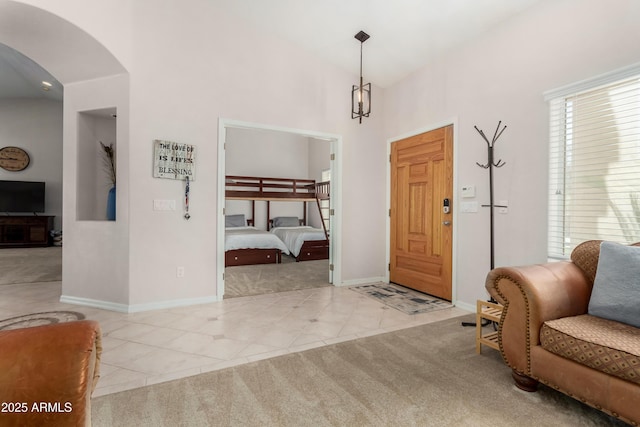 entryway featuring light carpet, light tile patterned floors, baseboards, arched walkways, and high vaulted ceiling