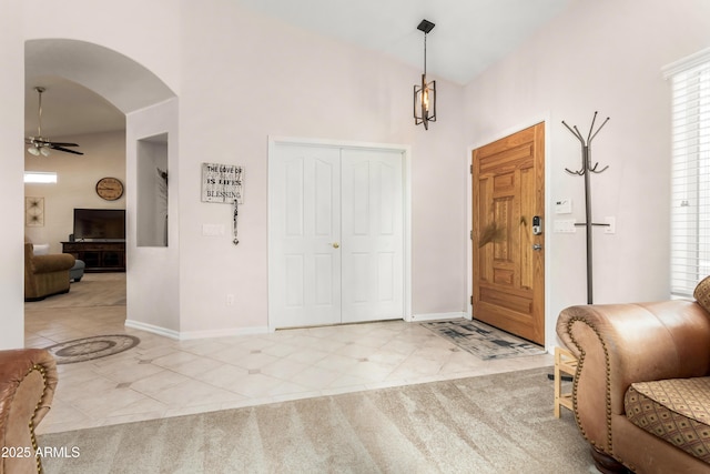 foyer entrance with arched walkways, light tile patterned flooring, a ceiling fan, and baseboards