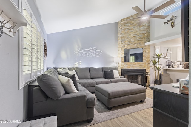 living room with ceiling fan, light hardwood / wood-style floors, high vaulted ceiling, and a stone fireplace