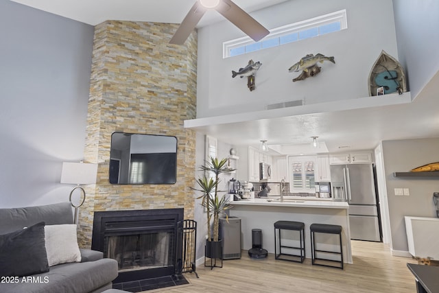 living room with sink, light wood-type flooring, a high ceiling, and a stone fireplace