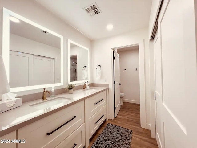 bathroom featuring vanity with extensive cabinet space, double sink, toilet, and hardwood / wood-style floors