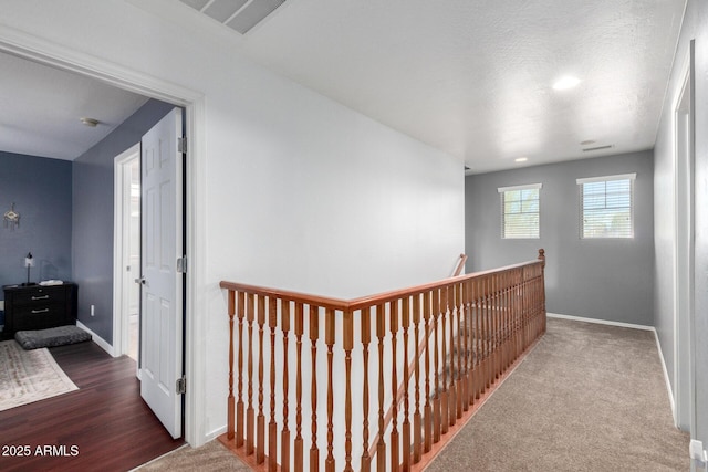 hallway with visible vents, baseboards, an upstairs landing, and carpet flooring