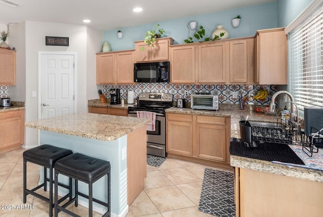 kitchen with light brown cabinetry, tasteful backsplash, stainless steel range with electric cooktop, light tile patterned flooring, and black microwave