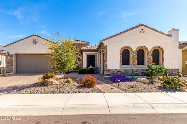 mediterranean / spanish house featuring an attached garage, a tile roof, decorative driveway, and stucco siding