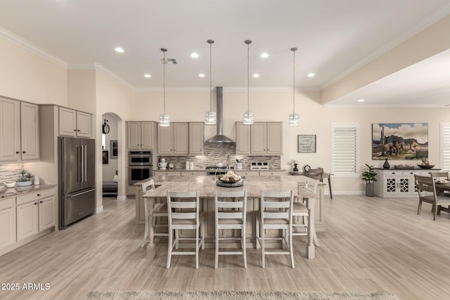 kitchen featuring light stone counters, arched walkways, stainless steel appliances, visible vents, and wall chimney exhaust hood