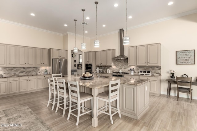 kitchen with a large island, a breakfast bar area, appliances with stainless steel finishes, a sink, and wall chimney exhaust hood