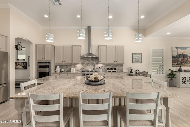 kitchen featuring visible vents, arched walkways, decorative backsplash, wall chimney exhaust hood, and stainless steel appliances