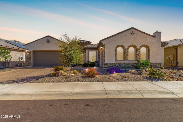 mediterranean / spanish-style house with stone siding, a tiled roof, an attached garage, decorative driveway, and stucco siding