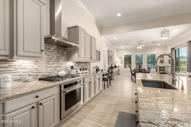 kitchen featuring tasteful backsplash, wall chimney exhaust hood, appliances with stainless steel finishes, crown molding, and a sink