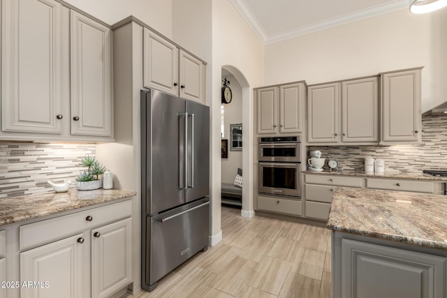 kitchen with arched walkways, stainless steel appliances, decorative backsplash, and ornamental molding