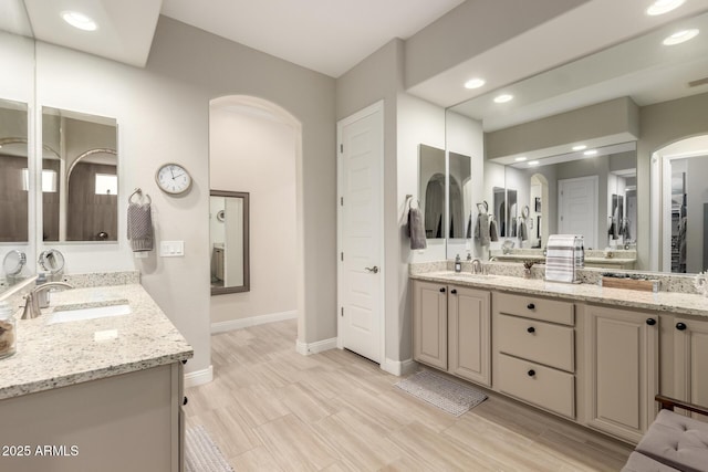 bathroom with baseboards, double vanity, a sink, and recessed lighting