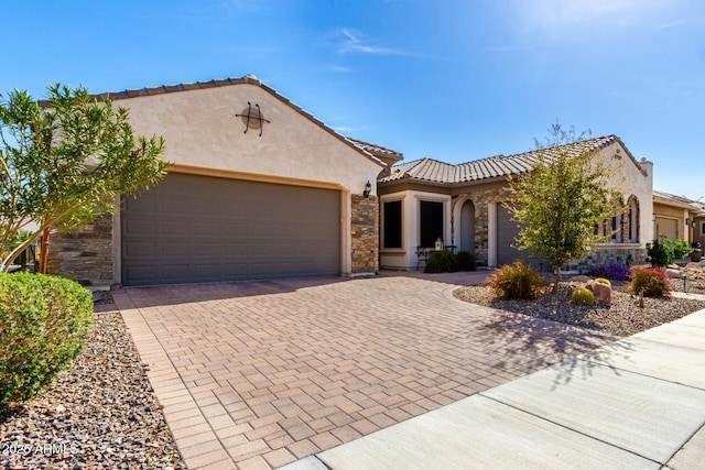 mediterranean / spanish home featuring stone siding, decorative driveway, an attached garage, and stucco siding