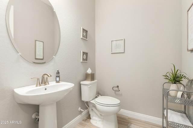 half bathroom with a sink, wood finished floors, toilet, and baseboards