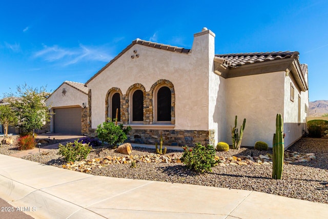 mediterranean / spanish-style house featuring a garage, a tiled roof, stone siding, stucco siding, and a chimney