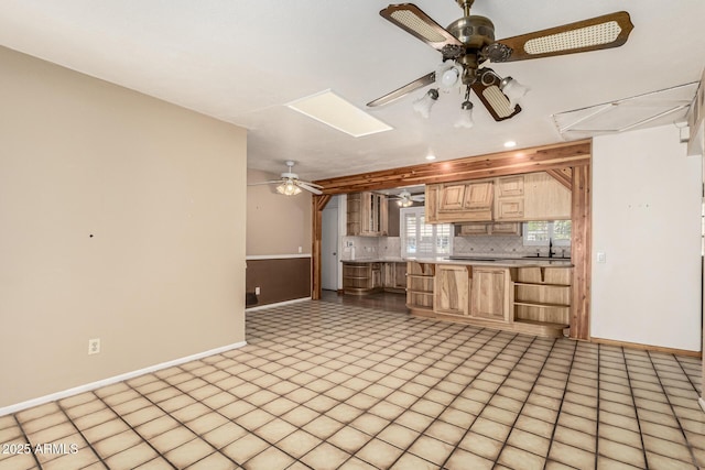 kitchen with light brown cabinetry, a skylight, light countertops, decorative backsplash, and ceiling fan