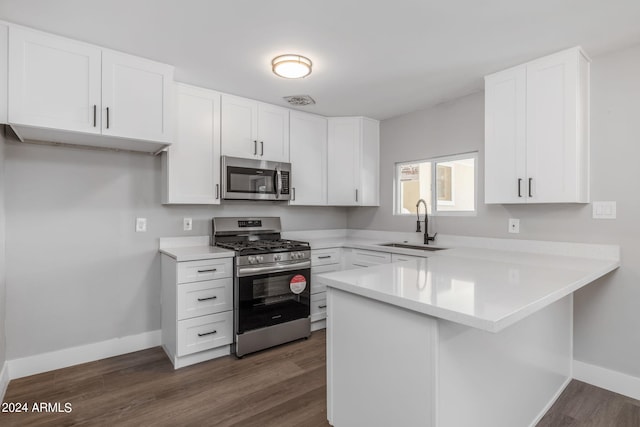 kitchen with kitchen peninsula, white cabinets, dark hardwood / wood-style flooring, appliances with stainless steel finishes, and sink