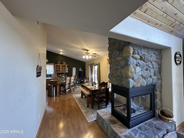 living area with vaulted ceiling, a ceiling fan, wood finished floors, and a fireplace