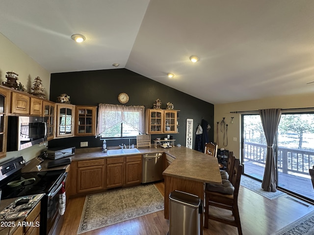 kitchen with a peninsula, vaulted ceiling, a kitchen bar, glass insert cabinets, and appliances with stainless steel finishes