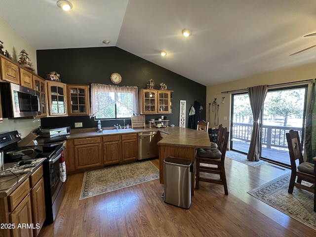 kitchen with a kitchen breakfast bar, vaulted ceiling, a sink, glass insert cabinets, and appliances with stainless steel finishes