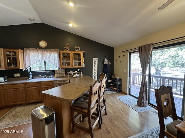 kitchen with vaulted ceiling, wood finished floors, a sink, glass insert cabinets, and a breakfast bar area