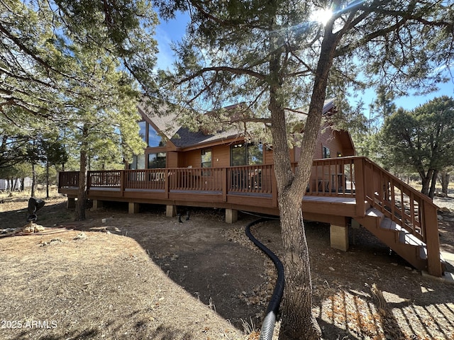 rear view of property featuring stairway, a wooden deck, and roof with shingles