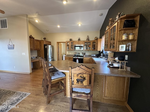 kitchen with stainless steel appliances, a sink, vaulted ceiling, visible vents, and brown cabinetry