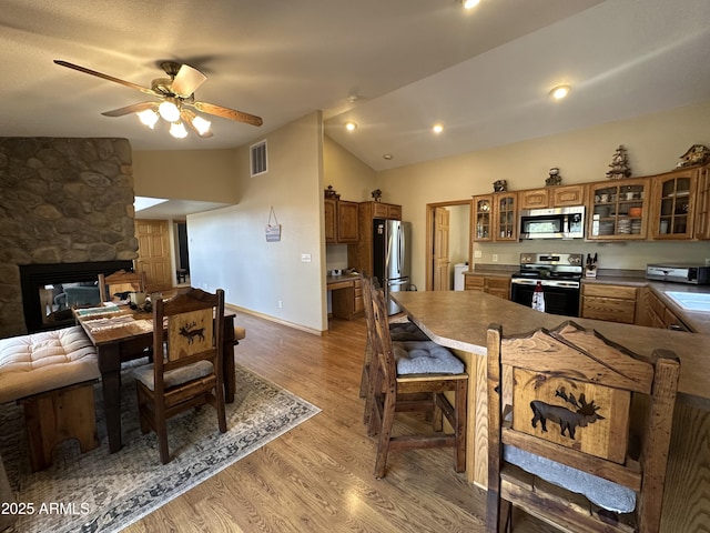 kitchen featuring brown cabinets, stainless steel appliances, vaulted ceiling, visible vents, and light wood-style floors