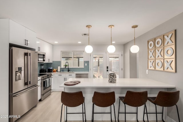 kitchen with sink, decorative light fixtures, a kitchen breakfast bar, stainless steel appliances, and white cabinets