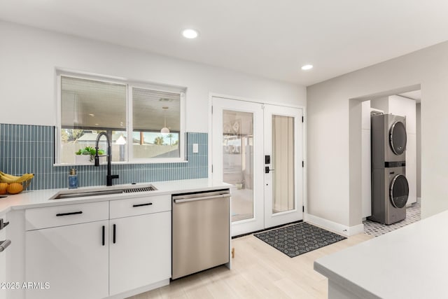 kitchen with sink, stainless steel dishwasher, white cabinets, and stacked washer / drying machine