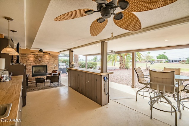 view of patio / terrace with area for grilling, a sink, a ceiling fan, an outdoor living space with a fireplace, and outdoor dining space